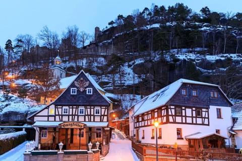 Striking half-timbered houses and mountain church in front of Mount Oybin with ruins, snow and