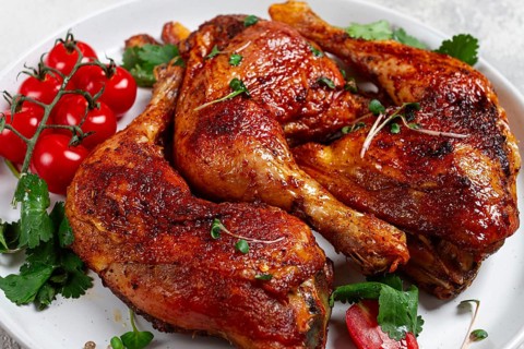 Grilled fried chicken legs, served, with fresh cherry tomatoes, and herbs, on a white plate,
