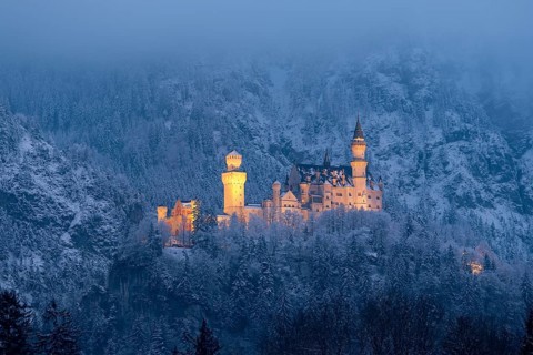 A magnificently illuminated castle at night, surrounded by a snow-covered landscape,