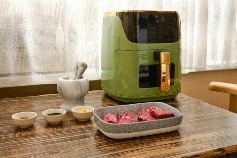 Fresh cuts of beef steaks sit on a wooden table next to bowls of spices and sauces ready to be