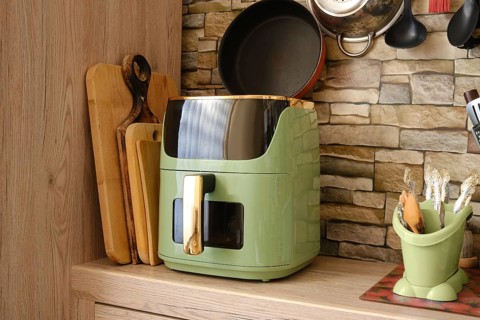 A green air fryer on a wooden kitchen counter, surrounded by cutting boards and kitchen utensils.
