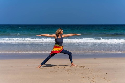 A woman doing yoga on a sandy beach by the sea. Virabhadrasana 2 or Warrior 2. Treen Cove,