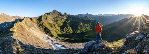 Mountaineer in front of mountain landscape at sunrise, sun star, view of mountain peaks of the