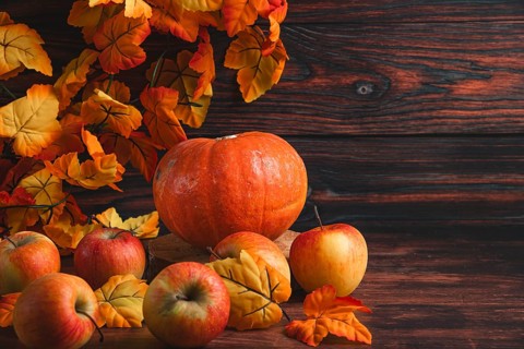 Autumnal arrangement with pumpkin and apples and colourful leaves on wood