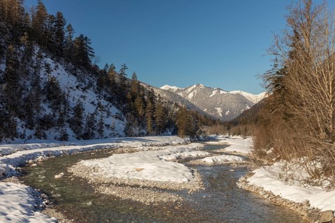 The Riss creek flowing through a snow covered landscape in the Eng valley. Sunny day with blue sky