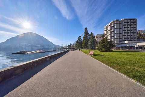 Lakeside promenade, lake, modern architecture, trees, backlight of the sun, blue sky with veil