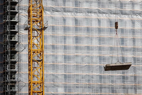 Essen, North Rhine-Westphalia, Germany - Construction crane lifts concrete section in front of