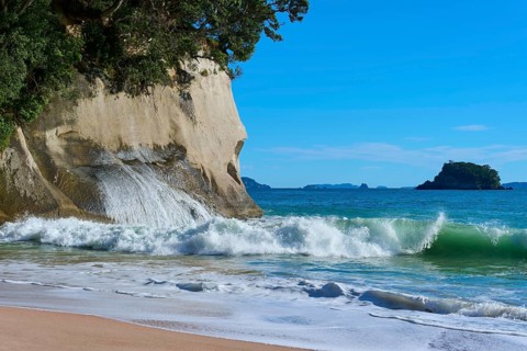 Waves crashing on a rocky coastline with splashing spray against a blue sea, Cathedral Cove, Hahei,