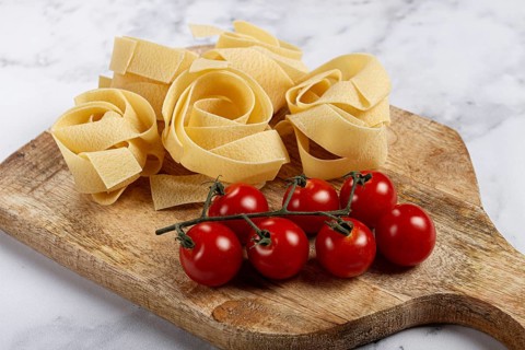 Raw pappardelle pasta, on a wooden chopping board, with cherry tomatoes, top view, no people