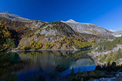 The Galgenbichl reservoir with a mountain forest in fall foliage on a bright sunny morning. Seen