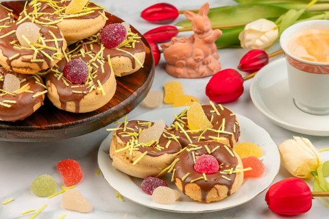 Decorated donuts next to coffee cup, Easter bunny, red tulips