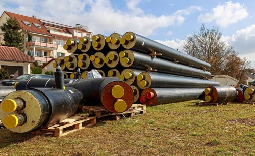 Stacked district heating pipes with yellow ends lie piled up in a meadow