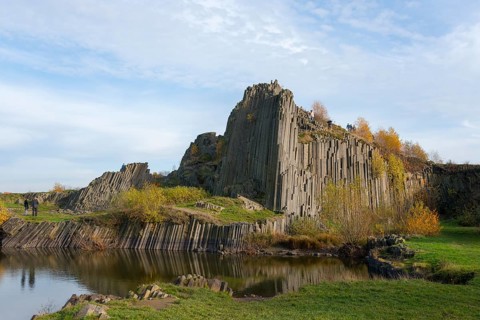 Mighty basalt formations rise under a blue sky, surrounded by autumnal greenery, manor house rocks,