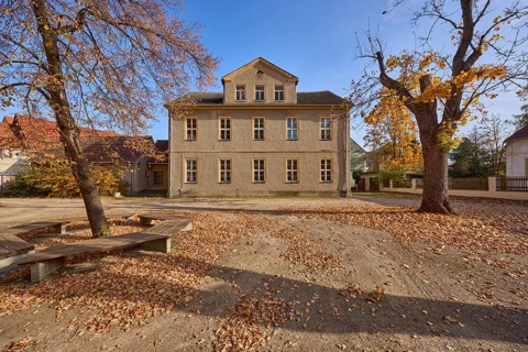 Two-storey building with pointed roof and dormer, autumnal trees, benches, school square, Mühlberg