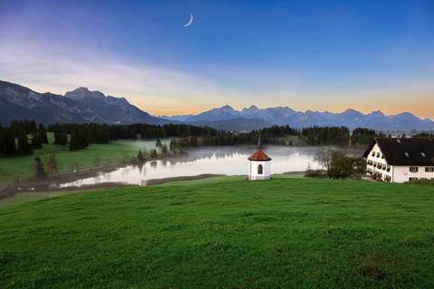Idyllic mountain landscape with chapel and lake in the evening light, peaceful atmosphere, crescent