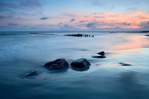 Sunset on the beach, boulders and old groyne in the surf, Klintholm Havn, Møn Island, Denmark,