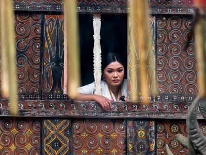 Woman dreamily at window, colourful old wooden house with carvings, Tana Toraja, Sulawesi,