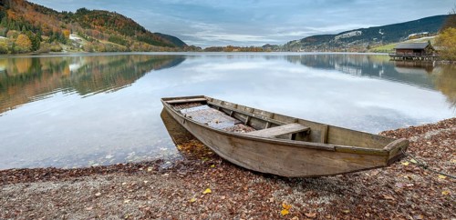 Traditional wooden rowing boat on the shore of Lake Schliersee in autumn, first snow on the slopes,