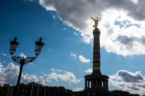 Victory Column next to an old street lamp in a dramatically cloudy sky with balu areas, towering