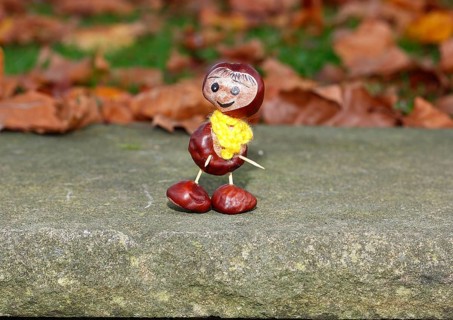 Funny chestnut figure with yellow scarf on a wall in autumn leaves, North Rhine-Westphalia,