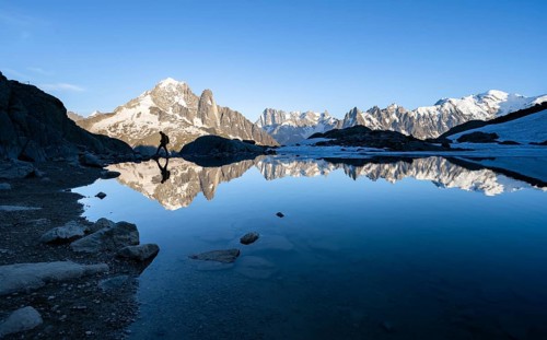 Mountaineer, silhouette in front of mountain landscape in the evening light, water reflection in