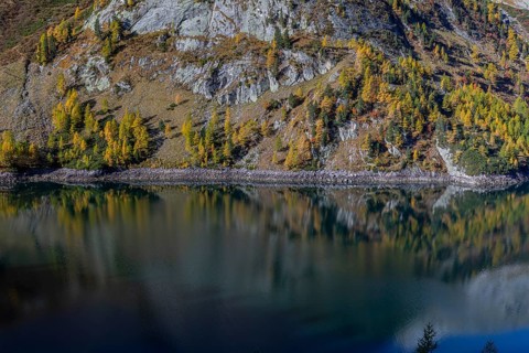 The Galgenbichl reservoir with a mountain forest in fall foliage on a bright sunny morning. Seen