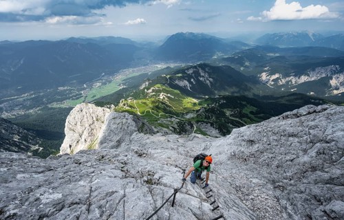Mountaineer with helmet climbing on the rock in a secured climb, on a narrow rocky ridge, in steep