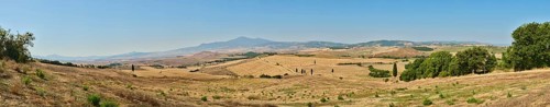 Typical Tuscan landscape in Val d'Orcia with hills, trees, fields, cypresses and farm road in