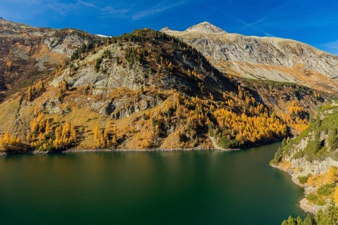 The Galgenbichl reservoir with a mountain forest in fall foliage on a bright sunny morning. Seen