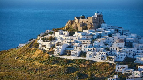 An ancient fortress overlooks a sea of houses on a hillside directly on the deep blue sea, Querini