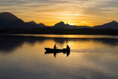 Two people in a boat on a lake at sunset, mountains in the background, Hopfensee, Hopfen am See,