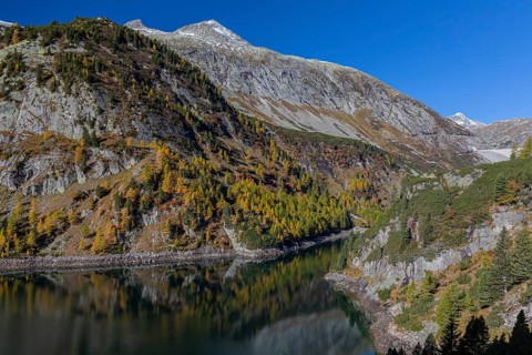 The Galgenbichl reservoir with a mountain forest in fall foliage on a bright sunny morning. Seen