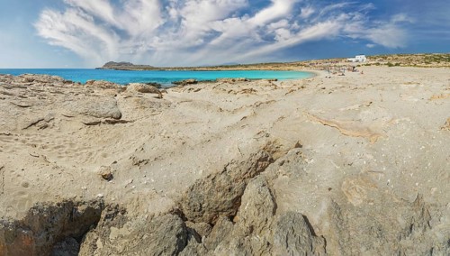 Rocks and sand meet the blue of the ocean under a wide, clear sky at Diakoftis Beach, Karpathos,