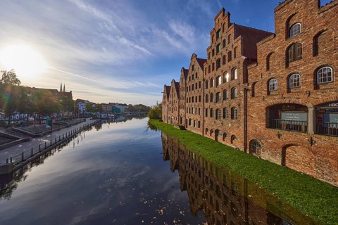 Historic salt warehouses, river Trave, blue sky with veil clouds in the backlight of the sun,