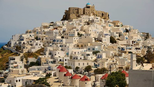 Whitewashed houses with red roofs and windmills under a stone castle, Querini Castle, Chora,