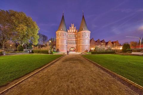 City gate Lübeck Holstentor, historic brick building, garden with lawn, trees, footpath made of
