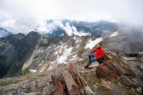 Mountaineer sitting on a rock, cloudy mountain landscape at the summit of Lasörling, view to Berger