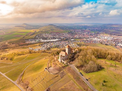 A castle stands above the fields and the village, surrounded by picturesque hills under a cloudy