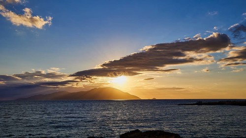 Dramatic sunset over the sea with clouds and island on the horizon, rays in the sky, sunset,
