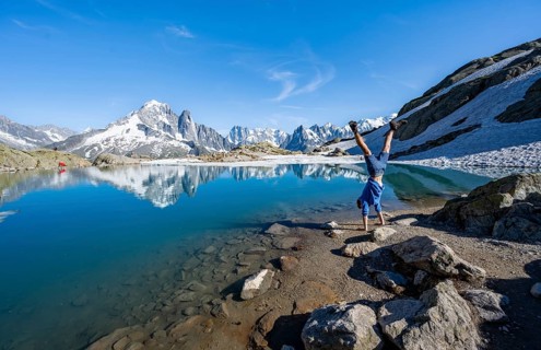 Young man doing a handstand, in front of mountain landscape with mountain lake, tourist at Lac