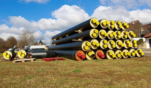 Stacked district heating pipes with yellow ends lie piled up in a meadow