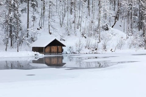 Snow covered boat shelter on Lake Almsee which is partly frozen and snow covered. Snow on the