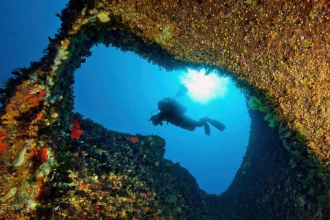Underwater photo with view through small tunnel breakthrough in rock reef on diver scuba diver in
