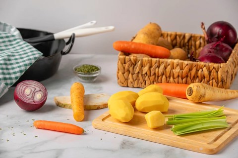 Peeled potatoes on a wooden board next to soup vegetables, preparation for cooking