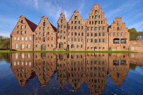 Historic salt warehouses with reflections on the water surface of the Trave, blue sky with veil