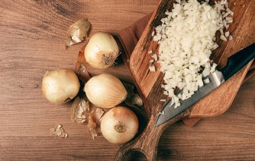 Finely chopped onion on a chopping board with a knife, wooden table, top view, no people