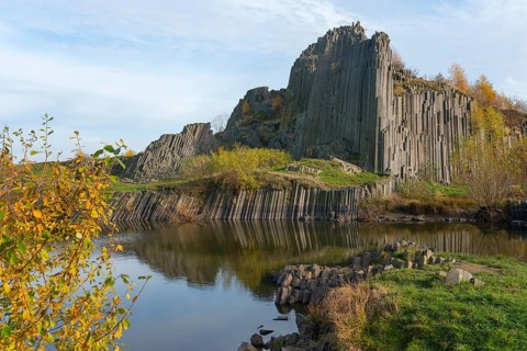 Impressive basalt columns are reflected in a quiet pond in autumnal surroundings, manor house
