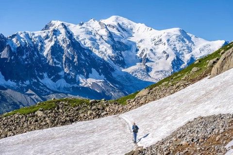 Mountaineer crossing a snowfield, view of spectacular glaciated peaks of Mont Blanc, Mont Blanc