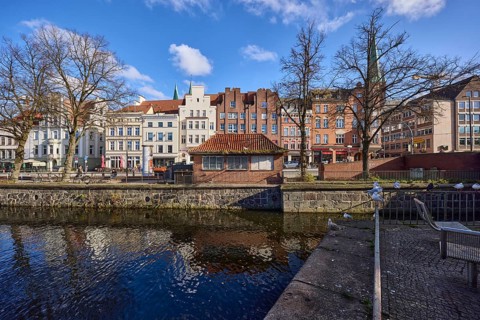 River Trave, historic houses, blue sky with fair weather clouds, quay wall, railing, street An der