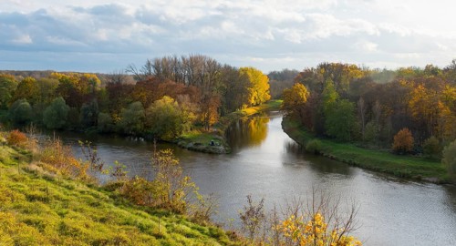 River, surrounded by autumnal trees and meadow landscape under a cloudy sky, confluence of the Elbe